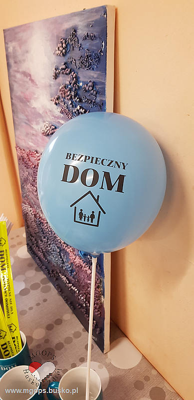 zdjęcie przedstawia balon w błękitnym kolorze z napisem BEZPIECZNY DOM oraz zarysem czteroosobowej rodziny stojącej w domu (MATERIAŁ PROMOCYJNY)